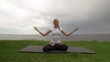 © stanis88 - Young fit woman practice yoga on coast near the lake or sea. Woman sitting in Knee Pile pose and meditating