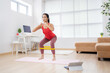 © torwaiphoto - Asian woman exercising at home on a yoga mat. She uses rubber resistance. She's doing squats.