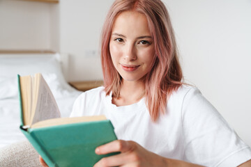 Sticker - Image of pleased pretty woman with pink hair reading book and smiling