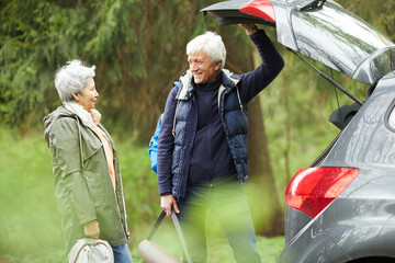 Wall Mural - waist up portrait of modern senior couple opening trunk of car and smiling happily while going on hi