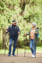 Wall Mural - full length portrait of active senior couple enjoying nordic walking with poles during hike in fores
