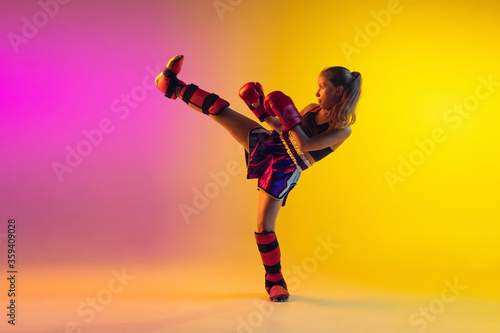 Fotografering Little caucasian girl, kick boxer on gradient background in neon light, active and expressive