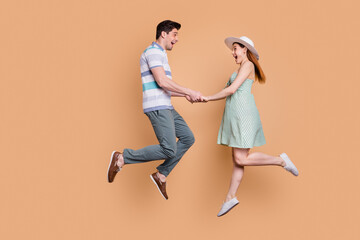 Wall Mural - Full length profile photo of attractive lady handsome guy funny married couple jumping high up good mood holding hands in love wear summer clothes isolated beige color background