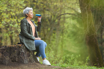 Wall Mural - side view portrait of active senior woman holding binoculars while enjoying hike in beautiful autumn