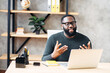© Vadim Pastuh - Video call. Attractive African-American guy is using laptop for video communication, a guy in glasses sits at the table in modern office, looking into webcam and talking online
