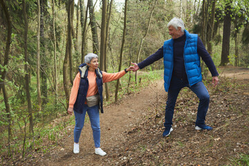 Wall Mural - full length portrait of active senior couple helping each other while climbing on hill during hike i