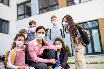 Canvas Print - Group of children, teacher with face masks outdoors at school after covid-19 lockdown.