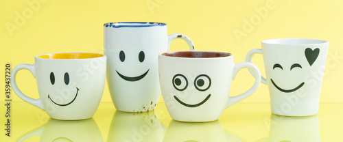 Four cups with funny faces on a color background. The concept of a friendly company, a big family, meeting friends for a cup of tea or coffee. Smiles on white coffee mug.