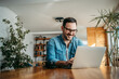 © bnenin - Portrait of a cheerful man using laptop while sitting at wooden table.