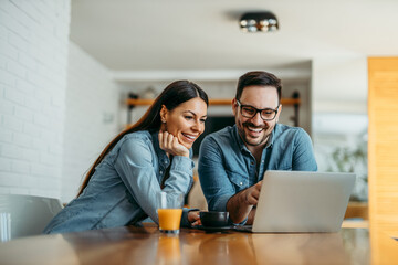 Portrait of a cute smiling couple looking at laptop together at home.