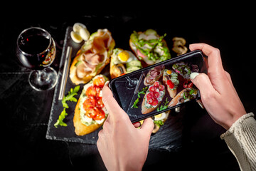 Wall Mural - Hands taking photo a italian bruschetta on a dark background with smartphone