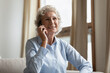 © fizkes - Middle-aged 55s woman sitting alone on sofa in living room holding smartphone enjoy pleasant conversation with relatives, grownup adult children or friend by distant talk using cell connection concept