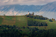 Jamnik church on hilltop with Alps mountains in background. Hill slope covered with grass and trees. Unique perspective of this famous picturesque church in Slovenia
