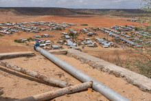 High Angle View On Water Supply In Melkadida Refugee Camp In Somali Region, Dollo Ado. Water Pipe In Foreground With Little Huts And Shelter, Desert And Hills In Background.