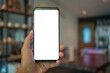 Close up of man hand holding mobile phone with white mock up blank copy space for your text message in cafe  with colorful lamp light and decorate furniture .Selective focus