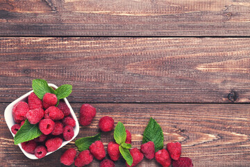 Poster - Sweet raspberries with green leafs in bowl on brown wooden table