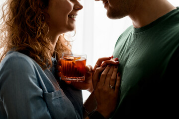 Smiling man and woman stand close together and hold one glass with cocktail.