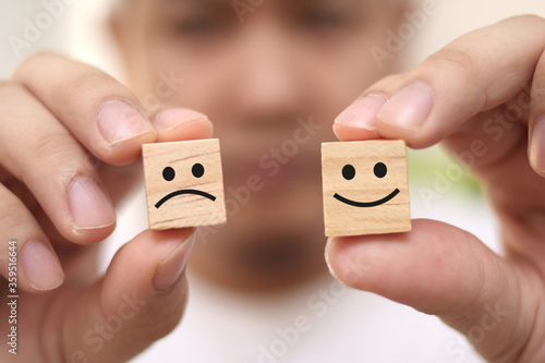 Life is a choice, be happy or sad concept, man holding wooden block with happy and sad face drawn on it