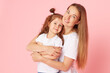 © oes - Mom and daughter in white t-shirts and jeans play and hug on a pink background. Caring for loved ones. Happy motherhood
