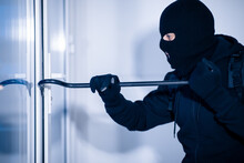 Robber In Black Balaclava Cracking Door With The Crowbar