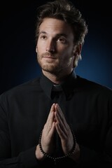 Wall Mural - Portrait of young handsome priest praying to God in dark room. 