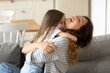 © fizkes - Close up happy attractive mother laughing hugging cute preschool daughter. Smiling young mom closed eyes embracing little girl playing in free time together sitting on couch at home.