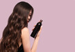 Beautiful brunette woman with curls and classic make-up in a black dress with a bottle of shampoo in hands. Beauty face.