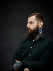Wall Mural - Studio portrait of a handsome tattooed man with stylish haircut posing on a dark background