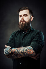 Wall Mural - Cool bearded guy with tattooed neck and hands posing in dark studio