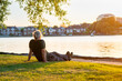 © okrasiuk - Back view gray hair mature man sitting on the green grass at the bank of park's lake and enjoying the sunset. A simple pleasure for mental health. Nature relaxation. Selective focus. Copy space.