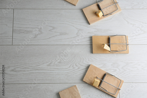 Fotografía Mousetraps with pieces of cheese and space for text on white wooden background, flat lay