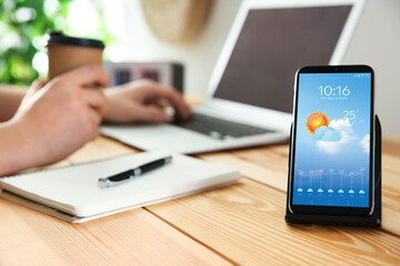 Wall Mural - man working at table and smartphone with open weather forecast app indoors