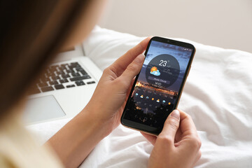 Wall Mural - woman using weather forecast app on smartphone at home, closeup