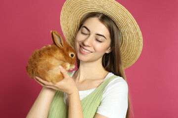 Wall Mural - Young woman with adorable rabbit on pink background. Lovely pet