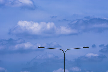 A street light with two lights on a pole stands against a blue sky with white clouds.