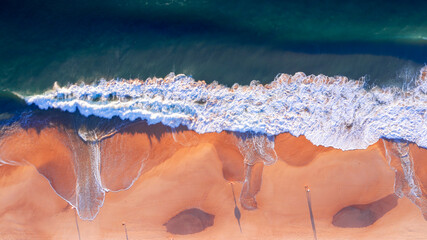 Top down aerial view over people walking on the beach with ocean waves