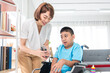 © jirakit - asian woman showing how to exercise with hand gripper to disabled child on wheelchair in living room
