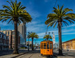 Old orange San Francisco cable car on the Embrcadero with the Ferry Building and palm trees in the background
