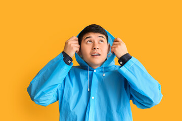 Wall Mural - Young Asian man in raincoat on color background