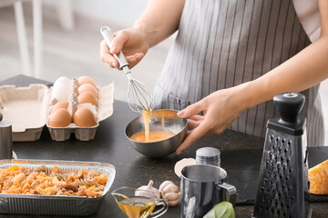 Woman preparing tasty pasta in baking dish on table