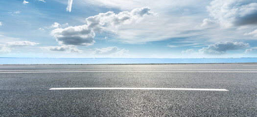 Asphalt road and lake water under blue sky.