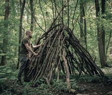 Man Building A Survival Shelter In The Forest. Shelter In The Woods From Tree Branches.
