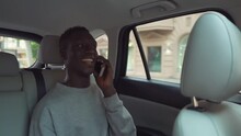Positive, Smiling African Man In Casual Clothes Talking On Cellphone While Riding In Backseat Of Taxi Cab. Cheerful Black Passenger Guy Answering Call Phone, Talking With Friends
