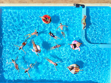 Aerial Of Friends Having Party In Swimming Pool With Inflatable Flamingo, Swan, Mattress. Happy Young People Relax At Luxury Resort On Sunny Day. View From Above. Girls In Bikini Sunbathing In A Sun.