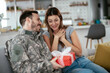 © JustLife - Soldier surprising his wife with a gift. Young man giving gift box to his girlfriend.