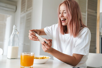 Wall Mural - Photo of woman playing online game on cellphone while having breakfast