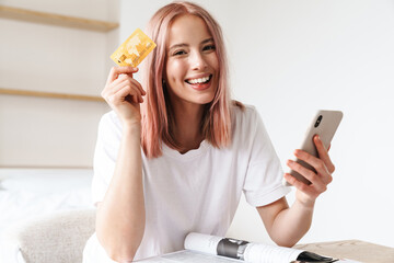 Wall Mural - Image of woman holding smartphone and credit card while doing homework