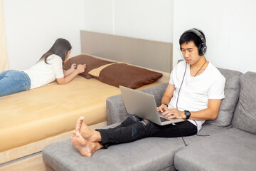 Asian men and women lover or couple using technology laptop with headphones.and mobile phone on the bed and sofa in bed room at modern home, , Lover concept,.