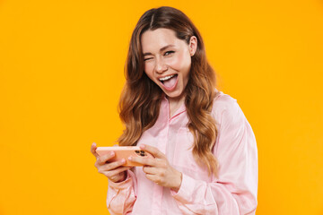 Poster - Image of cute pleased woman winking and playing video game on cellphone