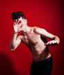 © iordani - young fashion style man with naked torso dancing emotional posing on red background, lifestyle people concept